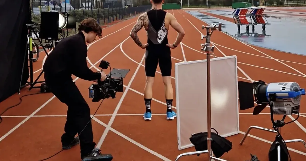 Vidéaste HUMAN REC filmant un athlète sur une piste, caméra à l'épaule et éclairage de tournage